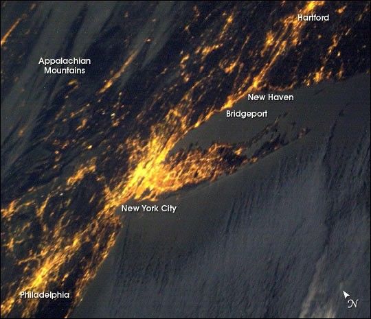 New York City at night from space, glowing with artificial light that hides the stars